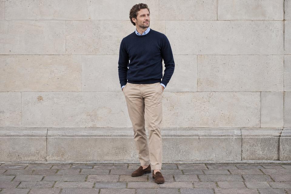 En mand i beige chinos, marineblå strik med lyseblå skjortekrave og brune loafers.