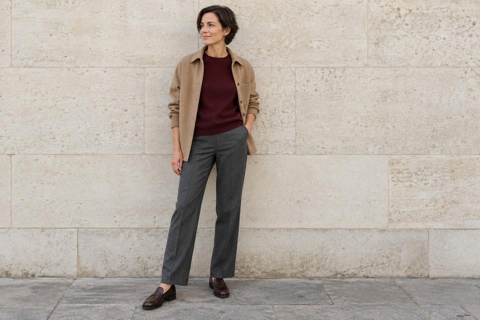 En kvinde i bordeaux strik, koksgrå bukser, åben camelfarvet overshirt og mørkebrune loafers.