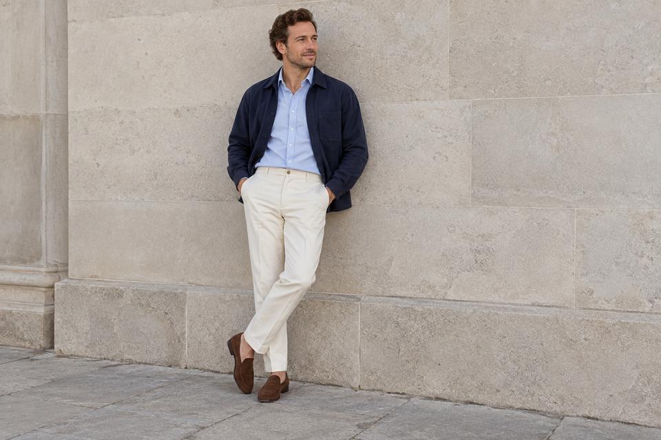 En mand i råhvide bukser, lyseblå skjorte, åben marineblå overshirt og brune loafers.